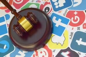 Wooden judge gavel lies on many paper logos of popular social networks and internet resources. Entertainment lawsuit concept photo