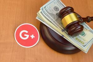 Google plus paper logo lies with judge gavel and hundred dollar bills. Entertainment lawsuit concept photo