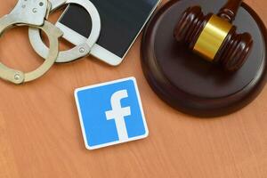 Facebook paper logo lies with wooden judge gavel, smartphone and handcuffs. Entertainment lawsuit concept photo