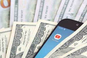 Smartphone screen with Youtube app and lot of hundred dollar bills. Business and social networking concept photo