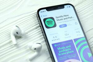 KHARKOV, UKRAINE - MARCH 5, 2021 Spotify icon and application from App store on iPhone 12 pro display screen with airpods pro on white table photo