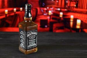 KHARKOV, UKRAINE - FEBRUARY 14, 2021 Jack Daniels No.7 whiskey bottle on wooden table with red bar interior on background. Elite alcohol photo