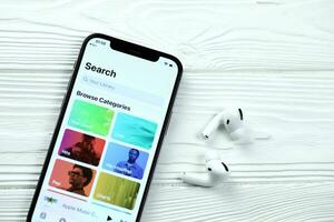 KHARKOV, UKRAINE - MARCH 5, 2021 Apple music icon and application from App store on iPhone 12 pro display screen with airpods pro on white table photo