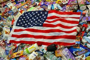 KHARKOV, UKRAINE - AUGUST 10, 2021 US flag on big pile of various wrappings and empty disposable packages and cups from famous branded food production photo