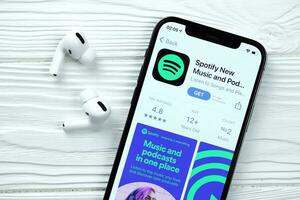 KHARKOV, UKRAINE - MARCH 5, 2021 Spotify icon and application from App store on iPhone 12 pro display screen with airpods pro on white table photo