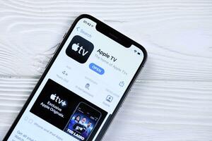 KHARKOV, UKRAINE - MARCH 5, 2021 Apple TV icon and application from App store on iPhone 12 pro display screen on white table photo