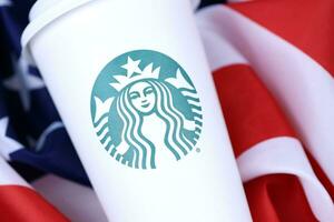 KHARKOV, UKRAINE - MARCH 15, 2021 Starbucks cup on US flag. Starbucks Corporation is multinational chain of coffeehouses headquartered in Seattle, Washington photo
