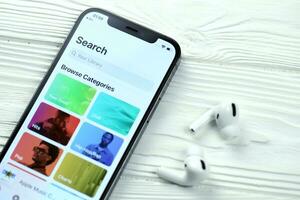 KHARKOV, UKRAINE - MARCH 5, 2021 Apple music icon and application from App store on iPhone 12 pro display screen with airpods pro on white table photo
