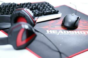 KHARKOV, UKRAINE - MARCH 14, 2021 A4tech bloody B3590R gaming keyboard, G501 headset and P93 optical mouse on B-070 Headshot surface in red and black colors photo