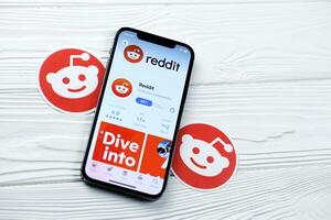KHARKOV, UKRAINE - MARCH 5, 2021 Reddit icon and application from App store on iPhone 12 pro display screen on white table photo