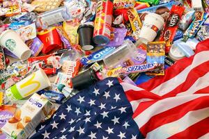 KHARKOV, UKRAINE - AUGUST 10, 2021 US flag on big pile of various wrappings and empty disposable packages and cups from famous branded food production photo