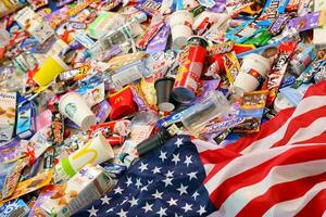 KHARKOV, UKRAINE - AUGUST 10, 2021 US flag on big pile of various wrappings and empty disposable packages and cups from famous branded food production photo