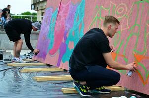 kharkov, ucrania - 27 de mayo de 2017 festival de artes callejeras. jóvenes dibujan graffiti en paredes portátiles de madera en el centro de la ciudad. el proceso de pintar en las paredes con latas de aerosol foto