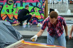 KHARKOV, UKRAINE - MAY 27, 2017 Festival of street art. Young guys draw graffiti on the car body in the city center. The process of drawing color graffiti on a car with aerosol cans photo