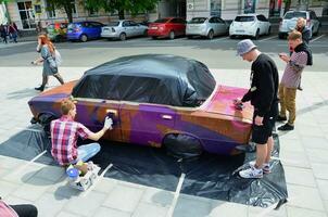 kharkov, ucrania - 27 de mayo de 2017 festival de arte callejero. los jóvenes dibujan graffiti en la carrocería del auto en el centro de la ciudad. el proceso de dibujo de graffiti de color en un coche con latas de aerosol foto