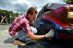 KHARKOV, UKRAINE - MAY 27, 2017 Festival of street art. Young guys draw graffiti on the car body in the city center. The process of drawing color graffiti on a car with aerosol cans photo