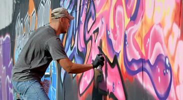 Young caucasian male graffiti artist drawing big street art painting in blue and pink tones photo