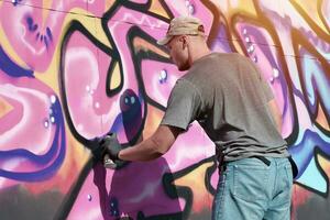 Young caucasian male graffiti artist drawing big street art painting in blue and pink tones photo