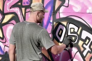 Young caucasian male graffiti artist drawing big street art painting in blue and pink tones photo