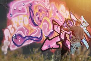 Young caucasian male graffiti artist drawing big street art painting in blue and pink tones photo