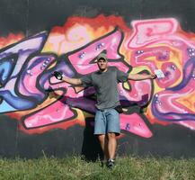 Young caucasian male graffiti artist drawing big street art painting in blue and pink tones photo