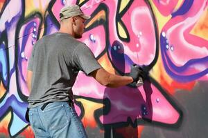 Young caucasian male graffiti artist drawing big street art painting in blue and pink tones photo