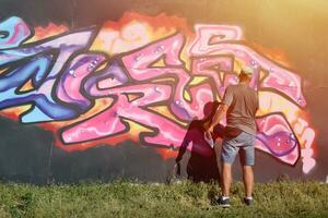 Young caucasian male graffiti artist drawing big street art painting in blue and pink tones photo