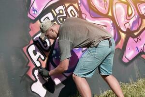 Young caucasian male graffiti artist drawing big street art painting in blue and pink tones photo