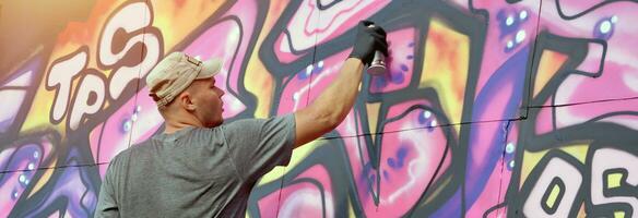 Young caucasian male graffiti artist drawing big street art painting in blue and pink tones photo