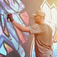 Young caucasian male graffiti artist drawing big street art painting in blue and pink tones photo