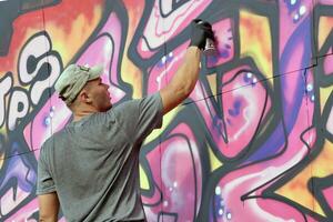 Young caucasian male graffiti artist drawing big street art painting in blue and pink tones photo