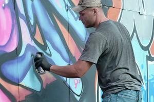 Young caucasian male graffiti artist drawing big street art painting in blue and pink tones photo