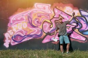 Young caucasian male graffiti artist drawing big street art painting in blue and pink tones photo