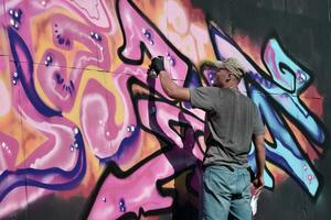 Young caucasian male graffiti artist drawing big street art painting in blue and pink tones photo