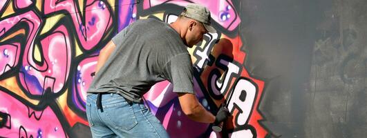 Young caucasian male graffiti artist drawing big street art painting in blue and pink tones photo