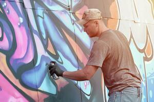 Young caucasian male graffiti artist drawing big street art painting in blue and pink tones photo