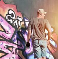 Young caucasian male graffiti artist drawing big street art painting in blue and pink tones photo