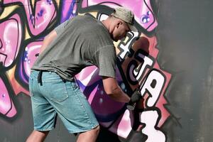 Young caucasian male graffiti artist drawing big street art painting in blue and pink tones photo