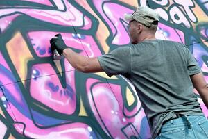 Young caucasian male graffiti artist drawing big street art painting in blue and pink tones photo