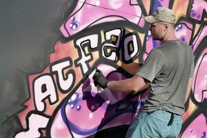 Young caucasian male graffiti artist drawing big street art painting in blue and pink tones photo