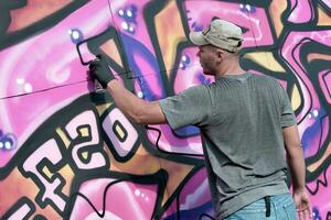 Young caucasian male graffiti artist drawing big street art painting in blue and pink tones photo