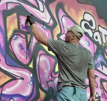 Young caucasian male graffiti artist drawing big street art painting in blue and pink tones photo