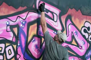 Young caucasian male graffiti artist drawing big street art painting in blue and pink tones photo