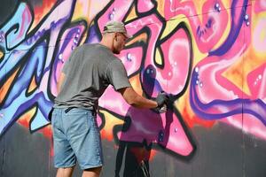 Young caucasian male graffiti artist drawing big street art painting in blue and pink tones photo