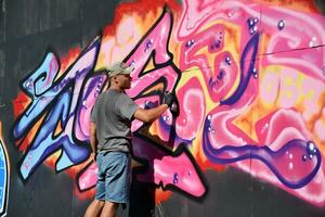 Young caucasian male graffiti artist drawing big street art painting in blue and pink tones photo