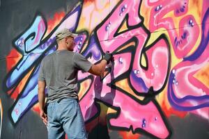 Young caucasian male graffiti artist drawing big street art painting in blue and pink tones photo