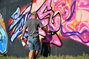 Young caucasian male graffiti artist drawing big street art painting in blue and pink tones photo