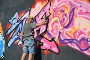 Young caucasian male graffiti artist drawing big street art painting in blue and pink tones photo