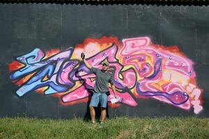 Young caucasian male graffiti artist drawing big street art painting in blue and pink tones photo