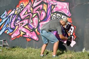 Young caucasian male graffiti artist drawing big street art painting in blue and pink tones photo